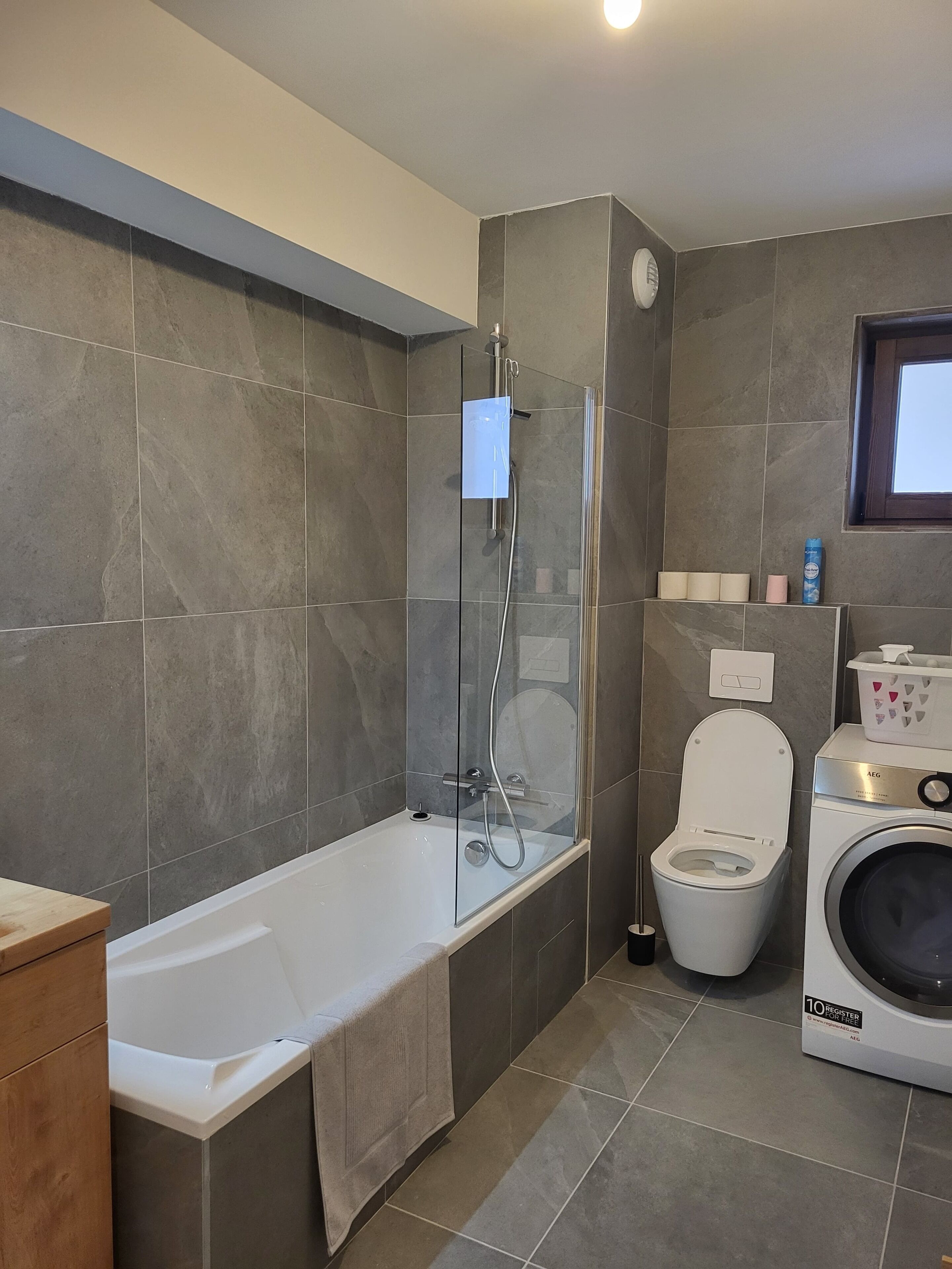 A modern bathroom with a bathtub, a glass-enclosed shower, a toilet, and a washing machine.