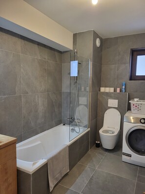 Ein modernes Badezimmer mit Badewanne, einer Glasduschkabine, Toilette und Waschmaschine.