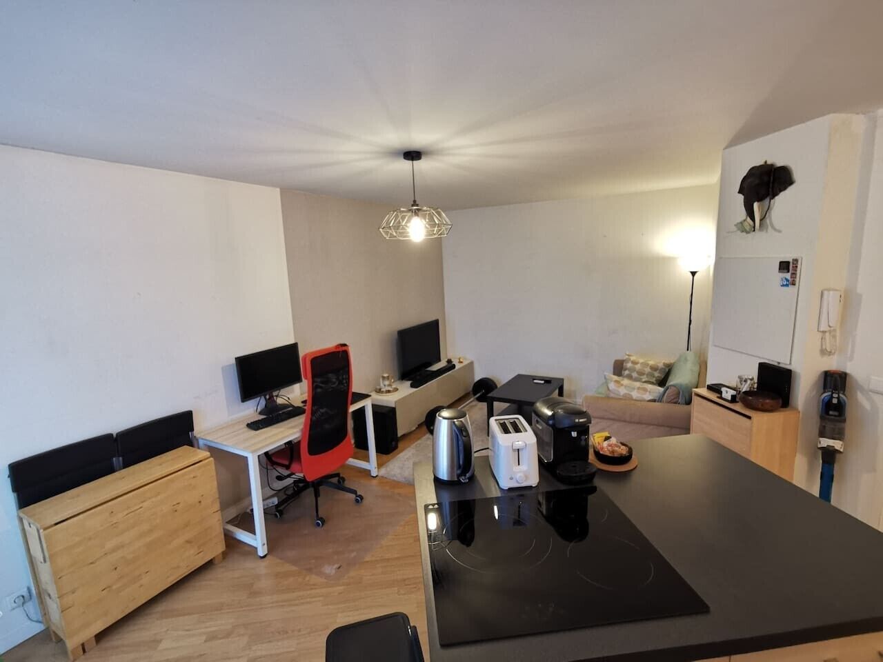 Un espacio habitable compacto con kitchenette, comedor, zona de trabajo con computadora y silla, y un pequeño rincón de descanso con sofá.
