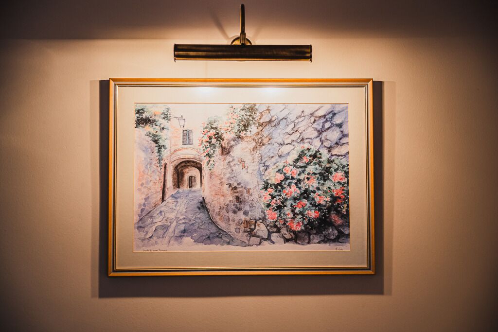 Un tableau encadré représentant une arche en pierre, avec un chemin et des plantes en fleurs, le tout sur un mur.