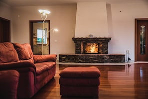 Ein Wohnzimmer mit Kamin aus Stein, einem roten Sofa und passendem Hocker.