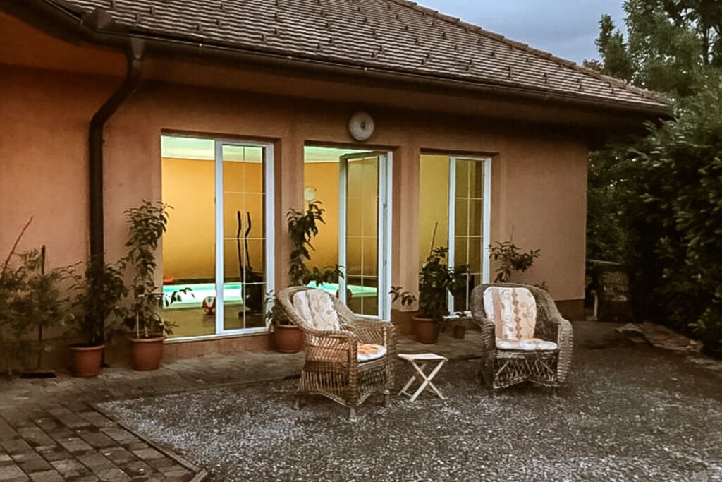 Un bâtiment avec un toit recouvert de tuiles, un patio comprenant deux chaises en osier et une petite table, ainsi que des plantes en pot disposées tout autour.