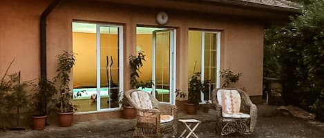 A building with a tiled roof, a patio area with two wicker chairs and a small table, and potted plants around.