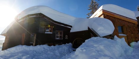 Une cabane en bois dont le toit est recouvert de neige, entourée de neige.