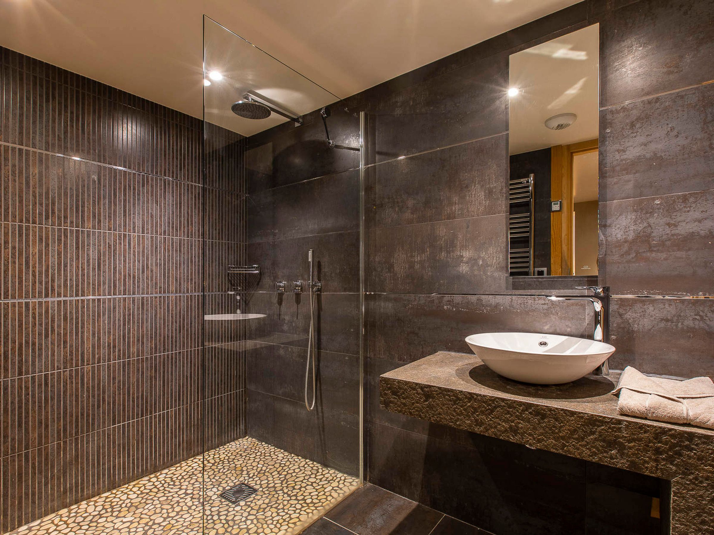 Un baño moderno con ducha de vidrio, lavamanos independiente y un espejo grande.