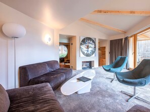 A modern living room with a dark brown sofa, a white coffee table, and a blue armchair. There is a large circular artwork on the wall and a wooden ceiling. - Exceptional chalet, central location - 10 guests (Avoriaz)