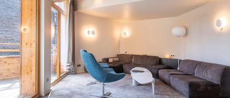 Una sala de estar moderna con un sofá seccional, un sillón azul y una pequeña mesa blanca.