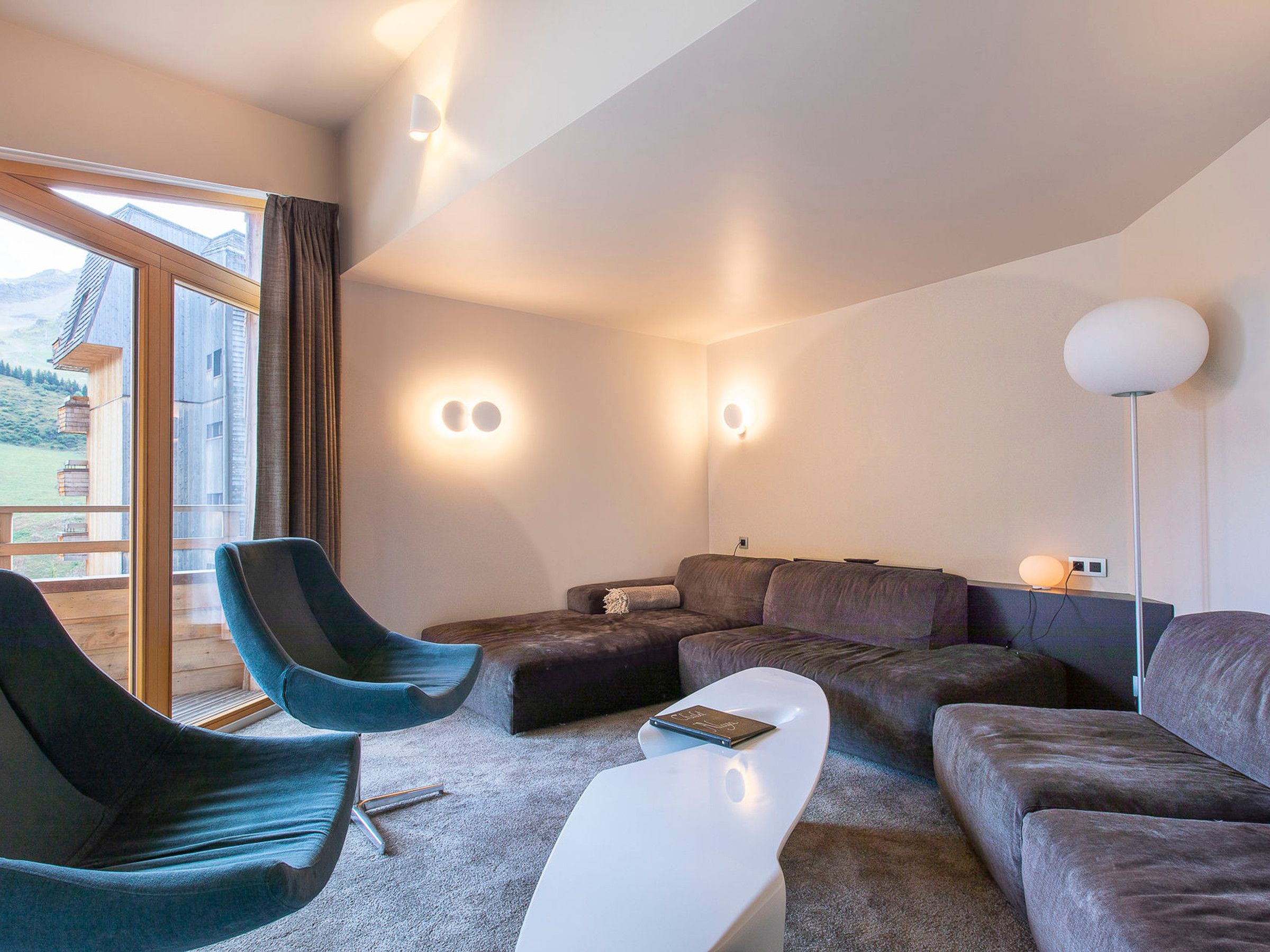 Een moderne woonkamer met een bank, fauteuil en salontafel. Twee wandlampen en een vloerlamp zijn zichtbaar.