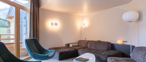 Una sala de estar moderna con sofá, sillón y una mesa de centro. Hay dos lámparas de pared y una lámpara de pie.