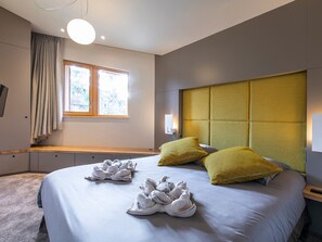 A modern hotel room with a large bed, a headboard with a textured panel, a window with curtains, and a bedside table with a remote control. - Exceptional chalet, central location - 10 guests (Avoriaz)