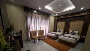 Habitación de hotel con dos camas, un escritorio, una silla, un televisor y un ventanal grande con cortinas.