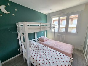 A room with a bunk bed, a single bed, a window with a view, and a wall with a crescent moon and stars. - Comfortable apartment near the beach - 5 guests (Les Sables-d'Olonne)