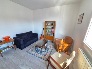 A living room with a sofa, a coffee table, a bookshelf, and a chair. - Comfortable apartment near the beach - 5 guests (Les Sables-d'Olonne)