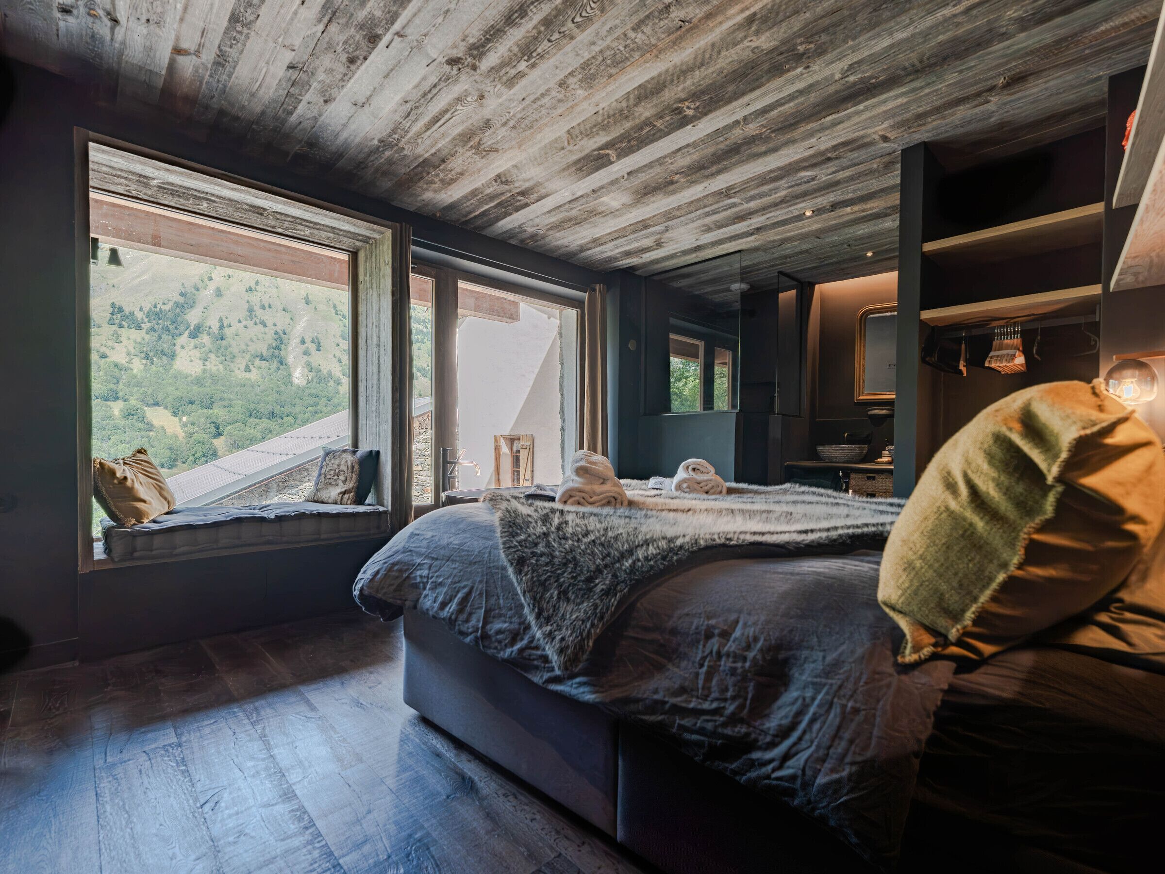 A bedroom with a large bed, a view of the outdoors, and a wooden ceiling.