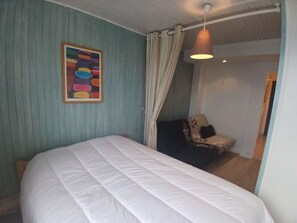 Ein Schlafzimmer mit einem Bett, einem Sessel, einem Gemälde und einer Pendelleuchte.