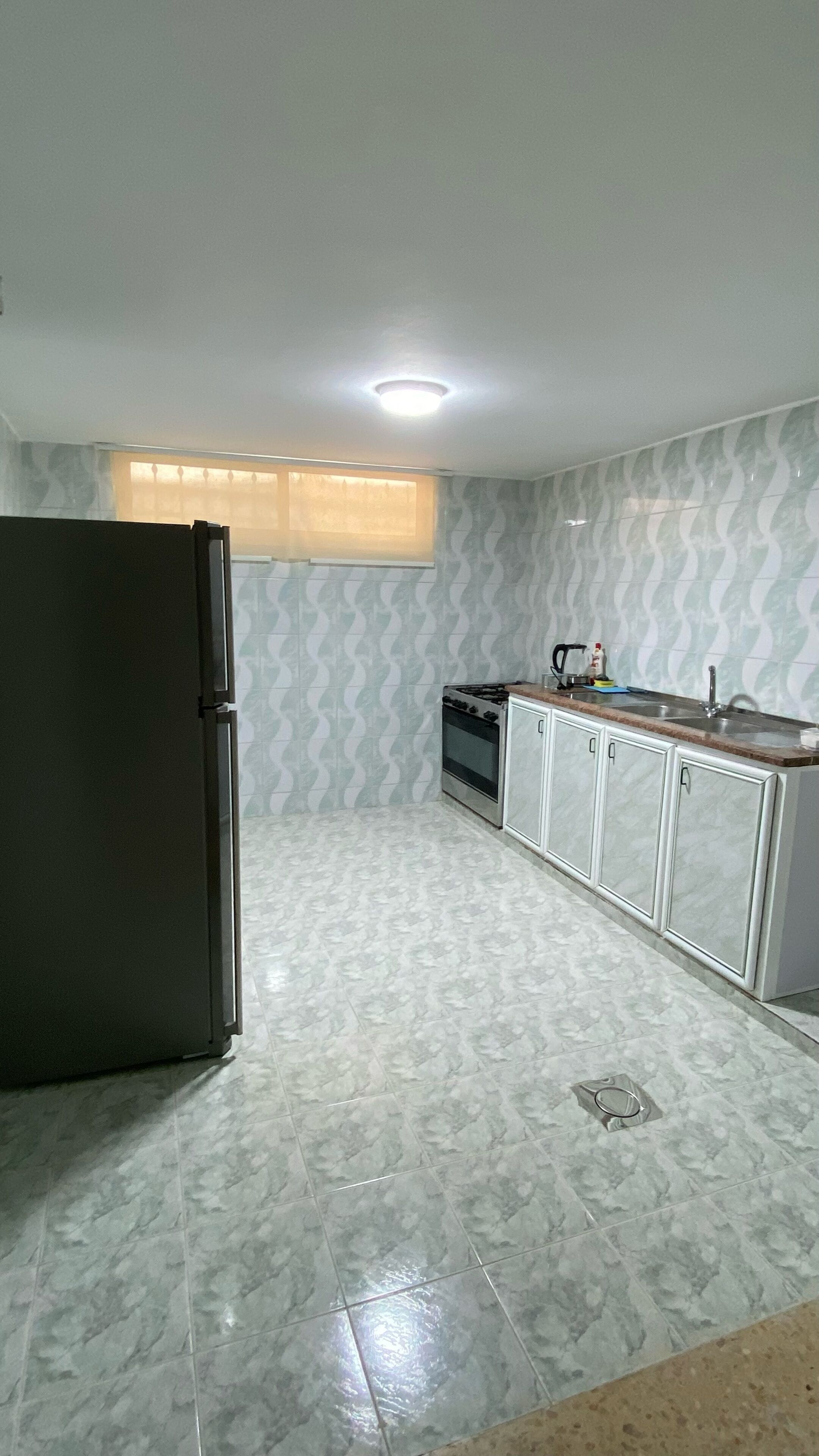 Eine Küche mit Kühlschrank, Herd, Schränken und einem Fenster mit Jalousien.