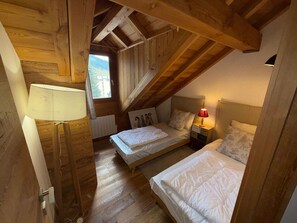 Quarto com duas camas, vigas de madeira, uma janela e um abajur.