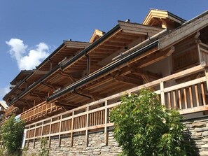 Ein traditionelles Holzgebäude mit Steinverkleidung, hölzernen Balkonen und blauem Himmel.