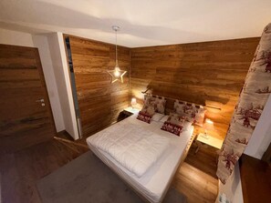 Une chambre avec une tête de lit en bois, un lit avec une literie blanche, un luminaire en forme d’étoile et une table de chevet avec une lampe.