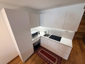Eine kleine Küche mit weißen Schränken, einer eingebauten Mikrowelle, einem Spülbecken und einem roten Teppich mit Muster.
