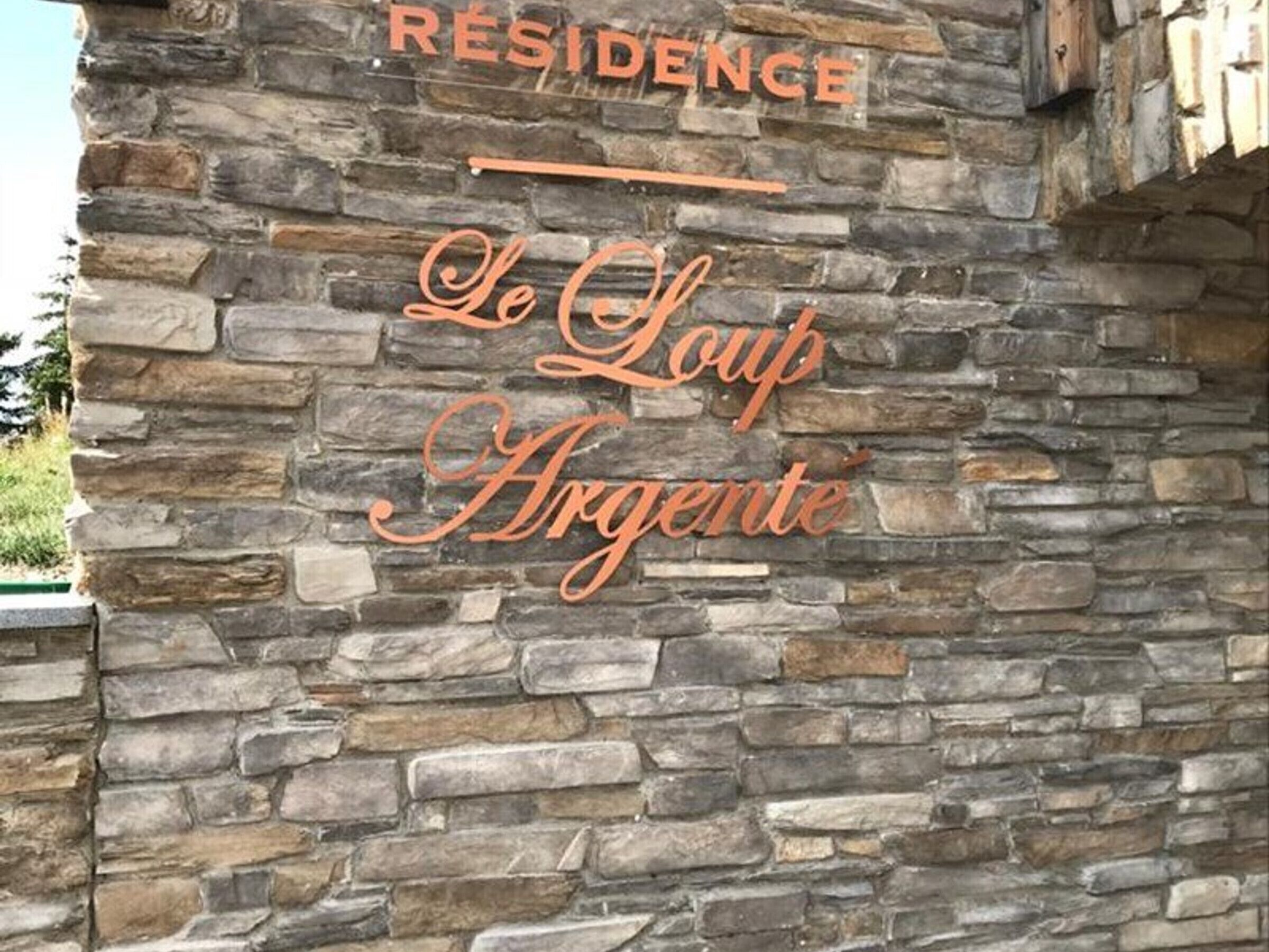 A stone wall with the text 'RESIDENCE Le Loup Argente' indicating a hotel or lodging establishment.
