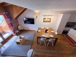 Ein Essbereich mit einem Holztisch, gedeckt für vier Personen, einem an der Wand montierten Fernseher und einer Küchenzeile mit Geräten.