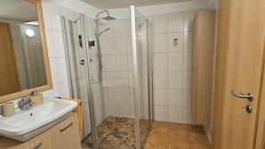 A bathroom with a glass-enclosed shower, a sink with a mirror, and a wooden door.