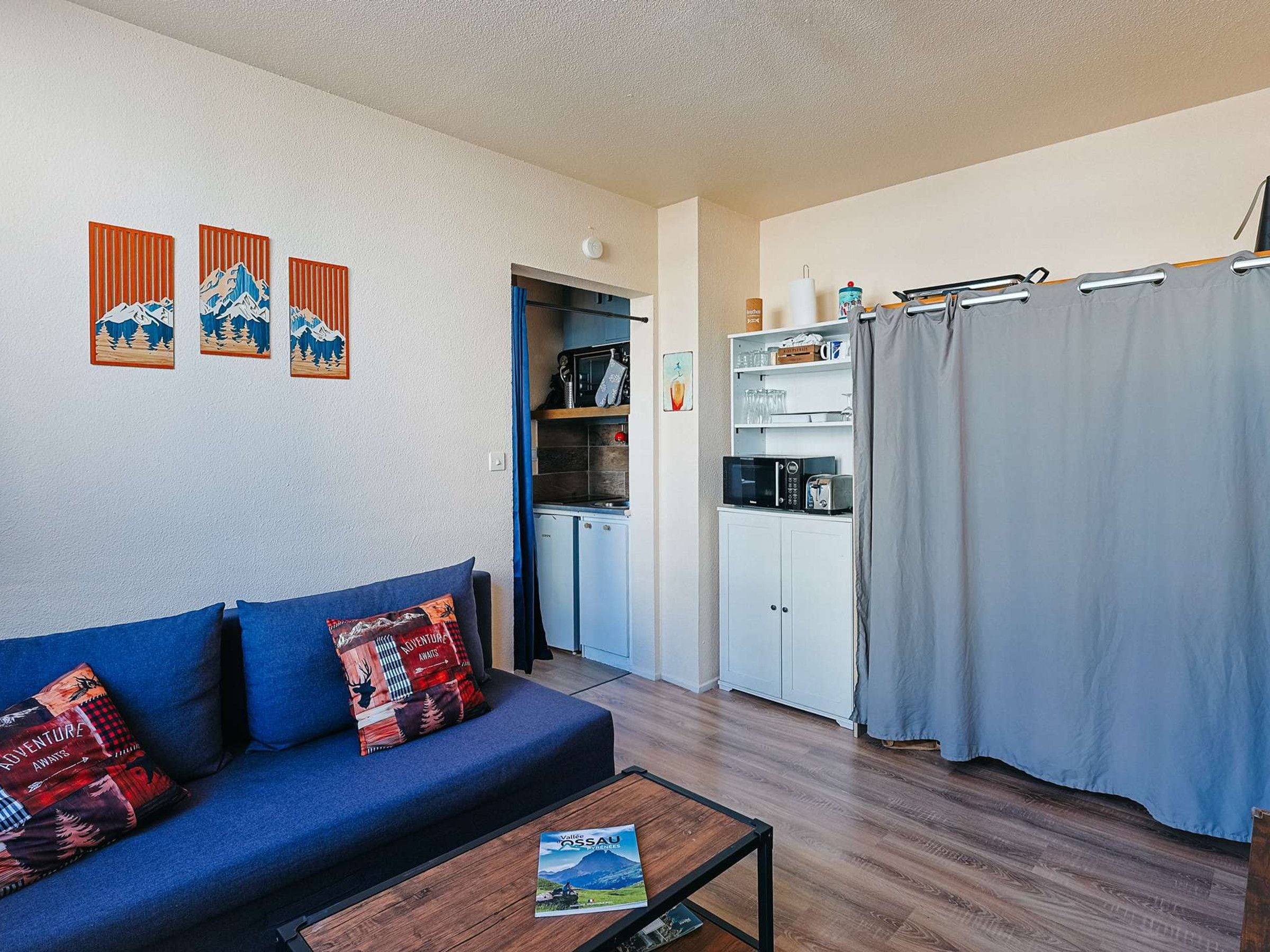 A compact living space with a sofa, a coffee table, a kitchenette, and a curtain.