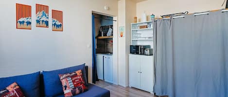 A compact living space with a sofa, a coffee table, a kitchenette, and a curtain.