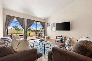 A living room with a sofa set, a coffee table, and a flat-screen TV mounted on the wall. - Rancho Mirage Vacation Condo | Panoramic Triple Fairway Views | Rancho Las Palmas Country Club (Rancho Mirage)
