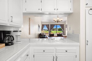 A modern kitchen with white cabinetry, a coffee machine, and a view of a patio with outdoor furniture. - Rancho Mirage Vacation Condo | Panoramic Triple Fairway Views | Rancho Las Palmas Country Club (Rancho Mirage)