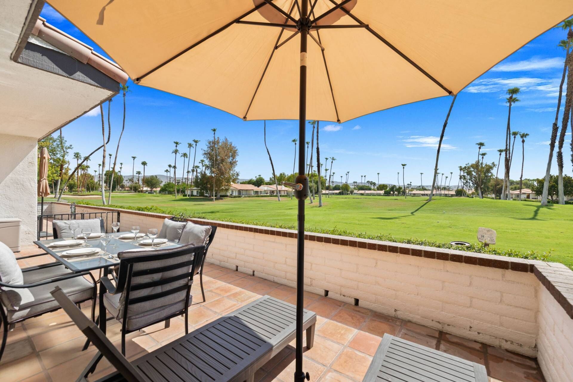 Une terrasse extérieure avec une table dressée pour le repas, un grand parasol et une vue sur un terrain de golf.