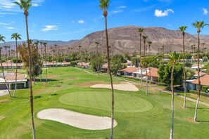 A golf course with sand bunkers, palm trees, and houses in the background. - Rancho Mirage Vacation Condo | Panoramic Triple Fairway Views | Rancho Las Palmas Country Club (Rancho Mirage)