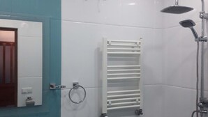 Un baño con lavamanos, espejo, toallero, ducha y ventana con persianas.