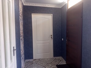 Un pasillo con piso estampado, una puerta blanca y una pared oscura.