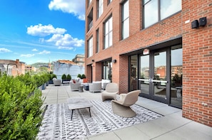 Eine Dachterrasse mit Sitzgelegenheiten im Freien, einem gemusterten Teppich und freiem Blick auf die Stadtlandschaft.