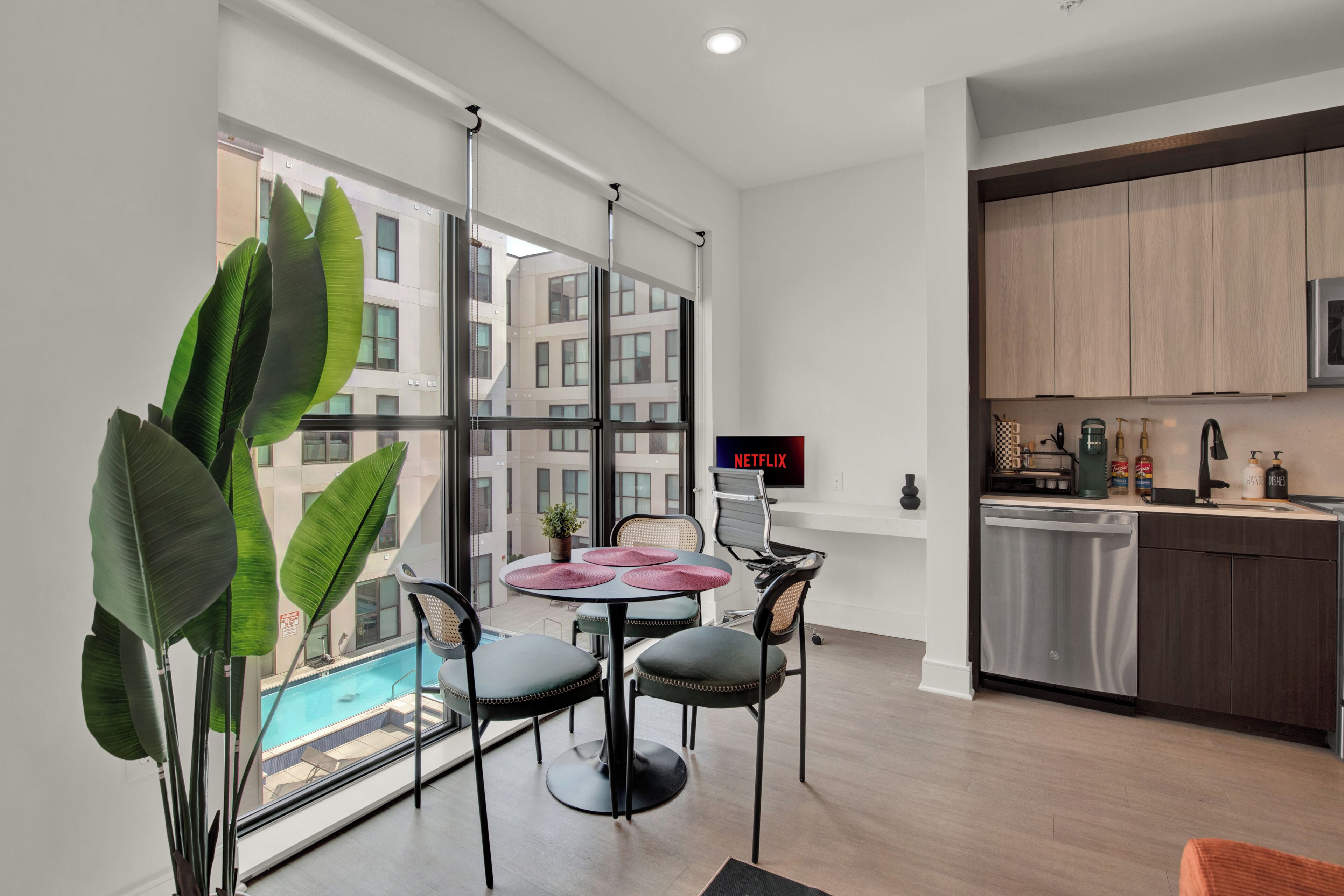 A modern kitchen with wooden cabinets, a built-in dishwasher, and a dining area with a round table and chairs.