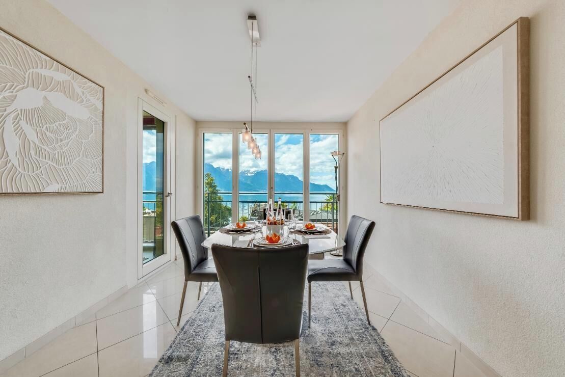 A dining area with a table set for four, large windows with a mountain view, and artwork on the walls.
