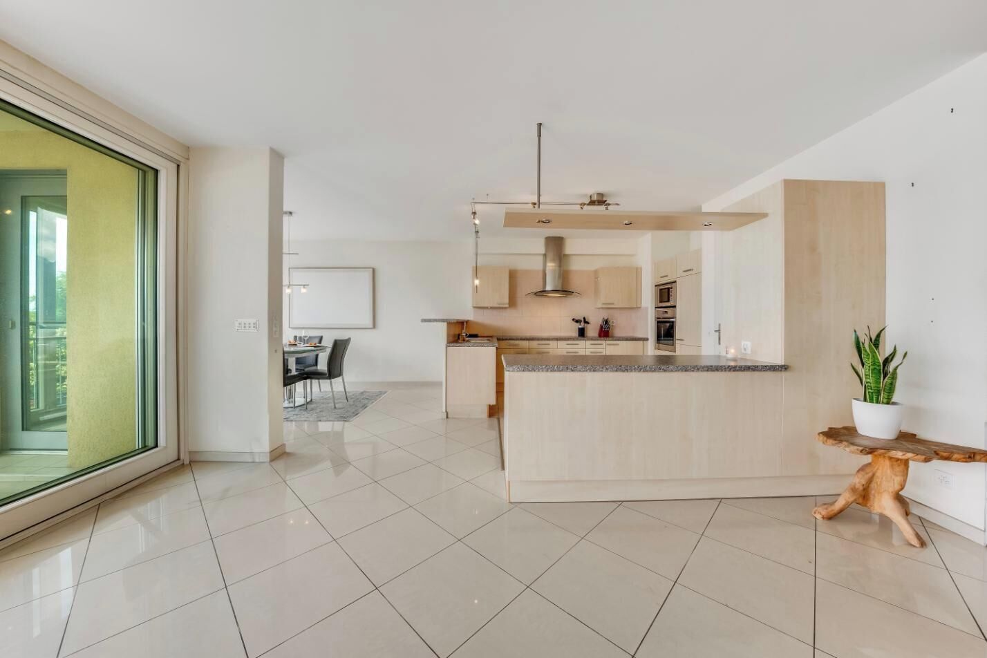 A modern kitchen with a central island, a dining area with a table and chairs, and a large sliding glass door leading to an outdoor area.