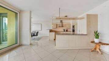 Uma cozinha moderna com uma ilha central, uma área de refeições com mesa e cadeiras, e uma grande porta de vidro deslizante que dá para uma área externa.