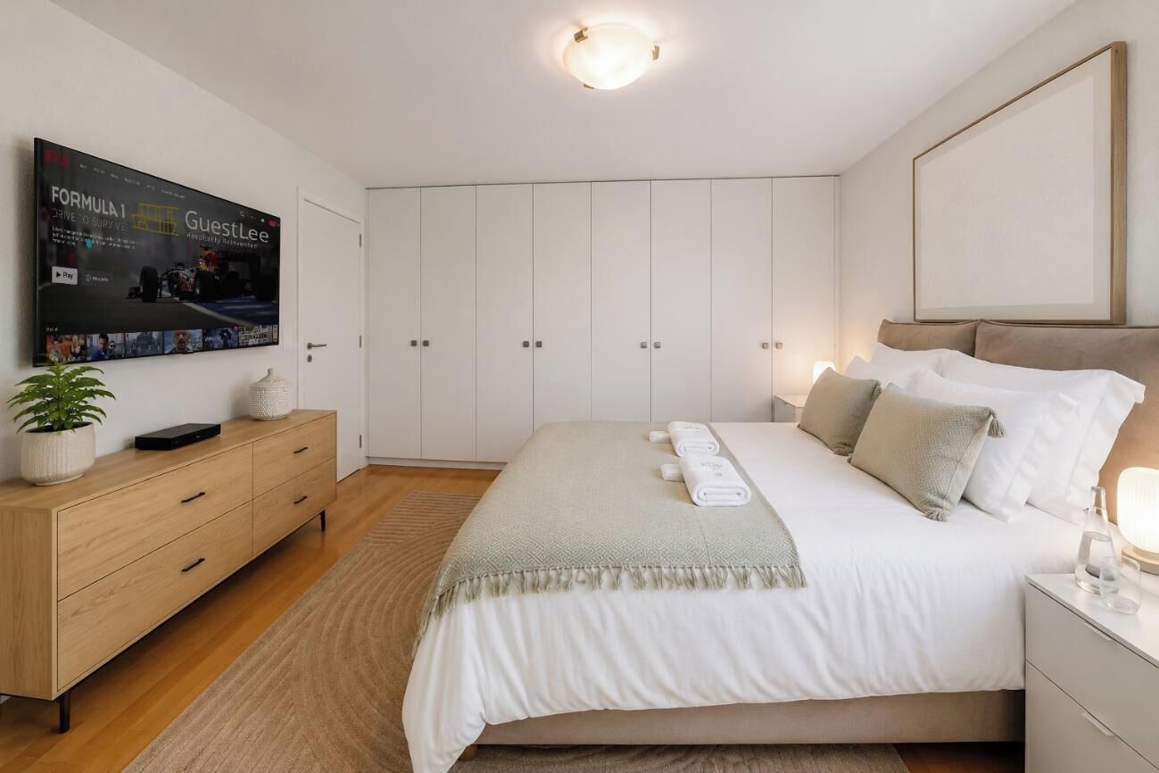 A modern bedroom with a bed, a TV mounted on the wall, a wardrobe, and a bedside table.