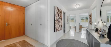 Un interior moderno con un pasillo que conduce a una sala de estar, con un armario de madera, una alfombra gris y un espejo grande.