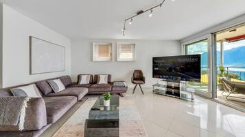 Un salon moderne avec un canapé d’angle, une table basse, un téléviseur à écran plat et un balcon offrant une vue sur la mer.