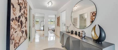 A hallway with a modern console table, a large mirror, and a framed abstract painting.