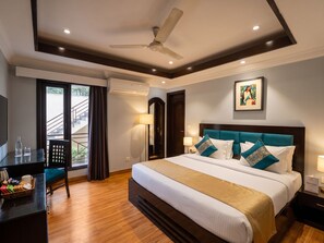 Habitación de hotel con cama, escritorio, silla, ventilador de techo y ventana con cortinas.