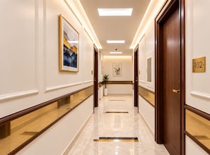 A hotel hallway with a marble floor, framed artwork on the walls, and a door with a number plaque. - asar Safdarjung By Orion Hotels (New Delhi)
