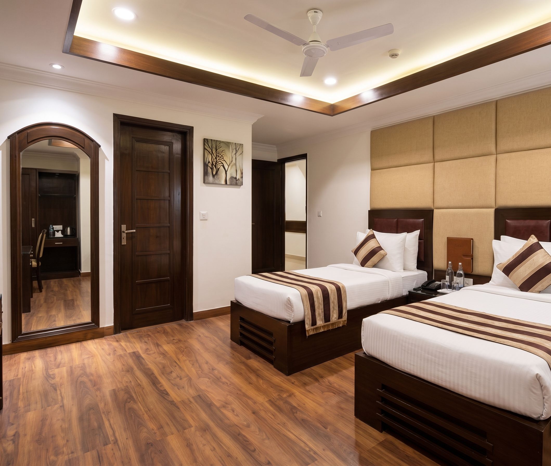 A hotel room with two beds, a ceiling fan, a wooden door, and a mirror.