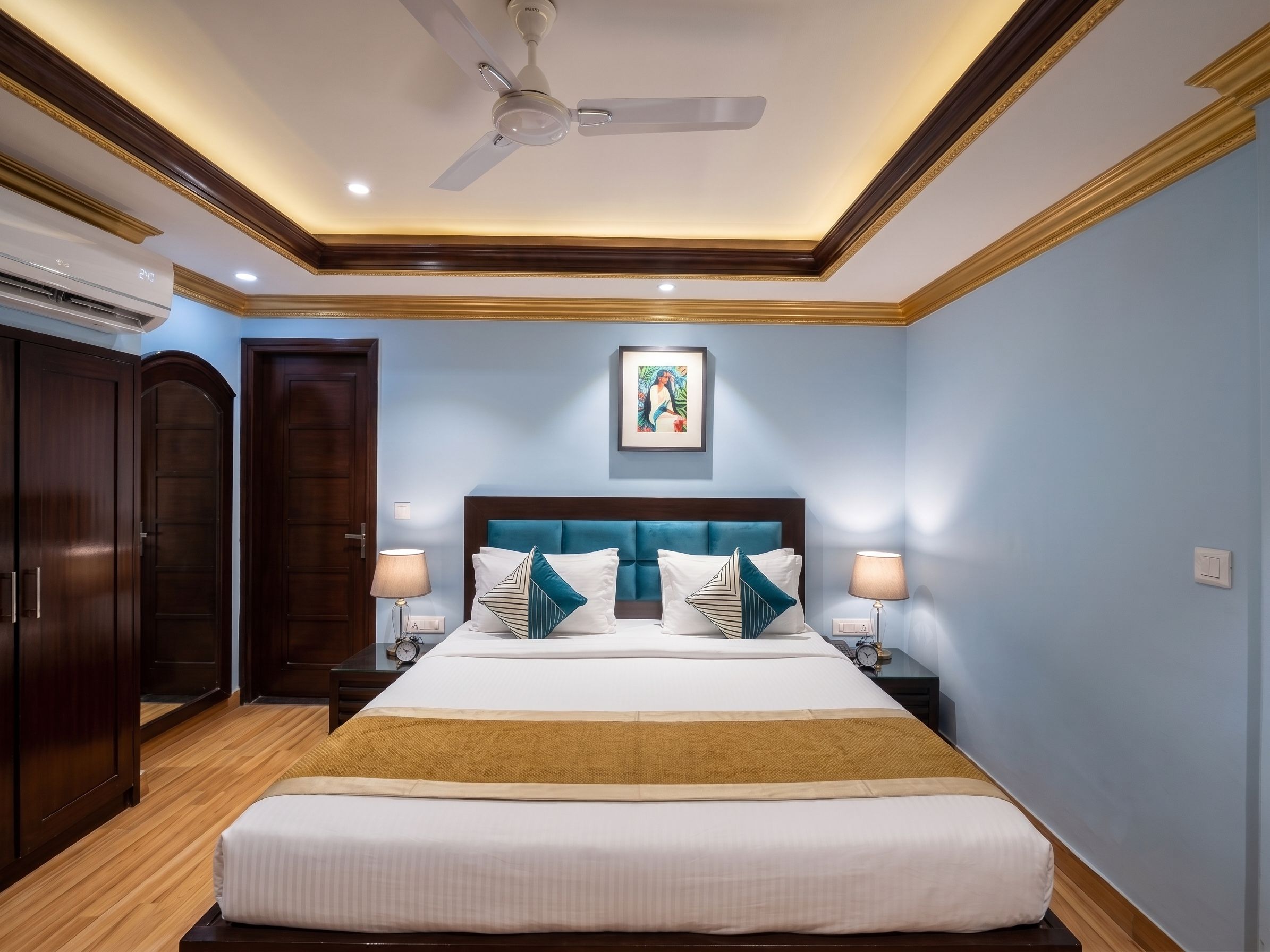 Una habitación de hotel con cama, mesitas de noche, ventilador de techo y un cuadro en la pared.