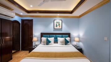 Une chambre d’hôtel avec un lit, des tables de chevet, un ventilateur de plafond et une œuvre d’art encadrée au mur.