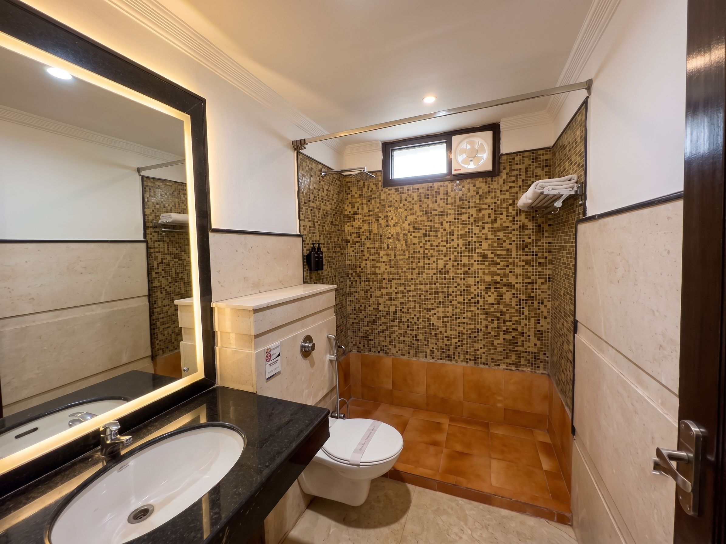 Un baño con pared de ducha revestida de azulejos, inodoro, lavabo con espejo y barra para toallas.